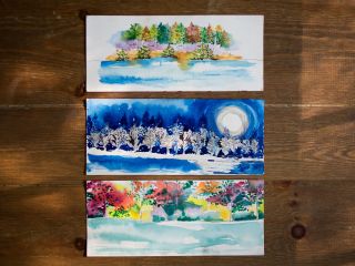 Three watercolor paintings sitting on a table at an art class at The Lodge at Woodloch