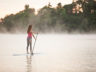 Solo woman stand up paddleboarding on the lake at sunrise at The Lodge at Woodloch
