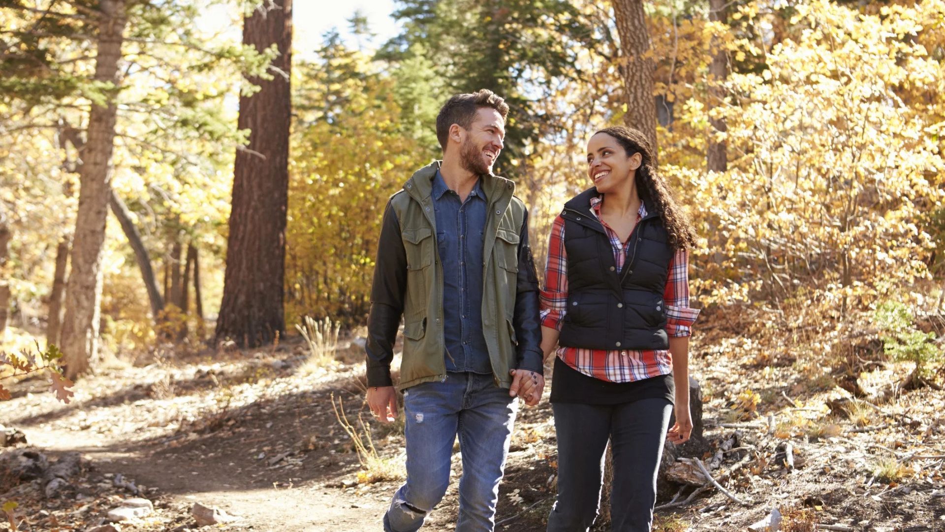A man and a woman holding hands on a wooded walk surrounded by Fall foliage