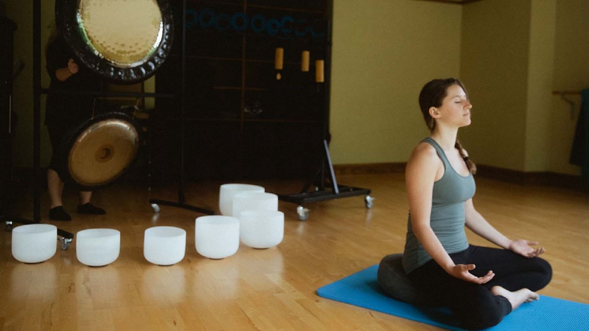 A woman meditation in front of crystal bowls and a gong