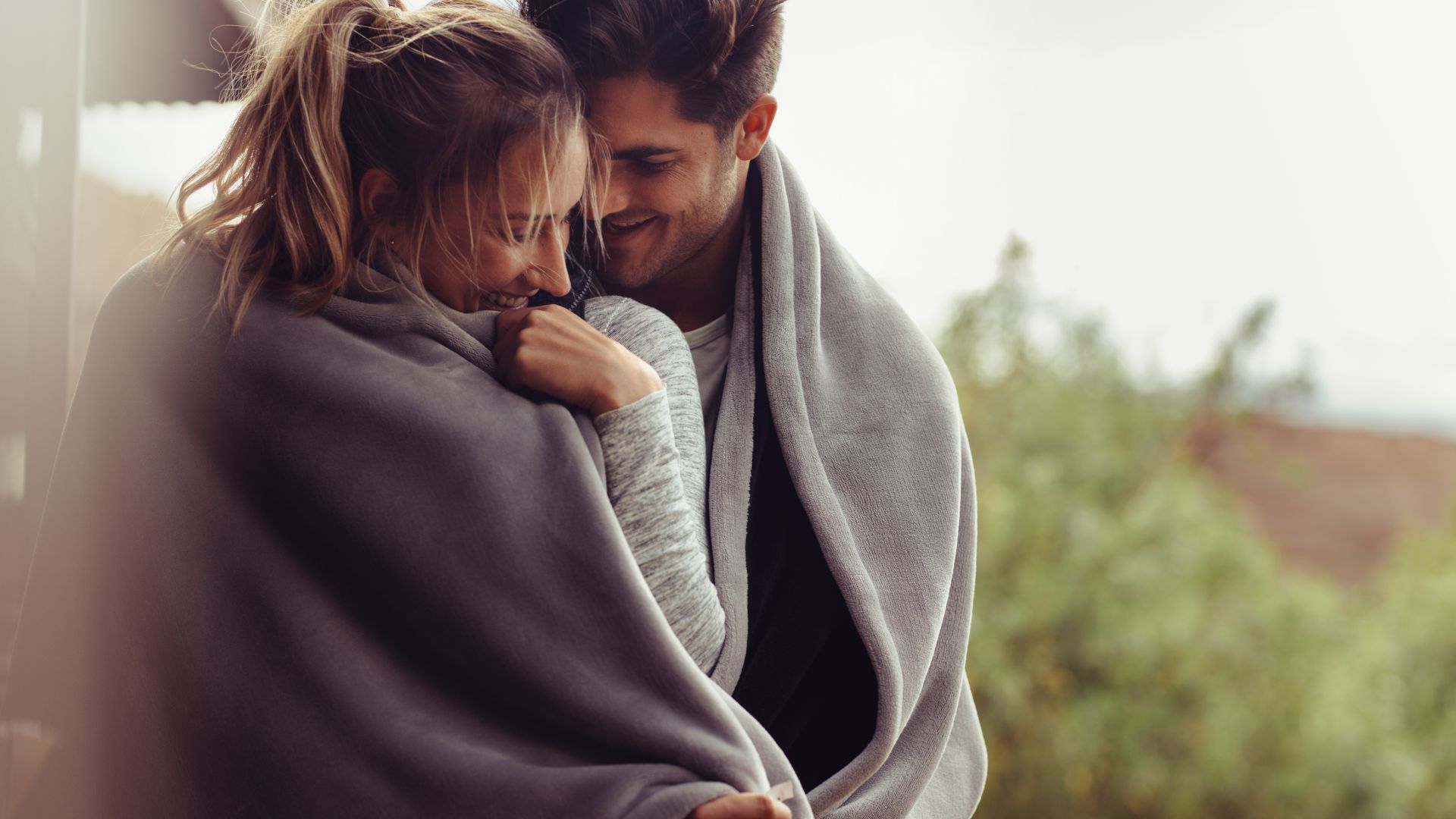 A man and a woman wrapped in a blanket outside of a building
