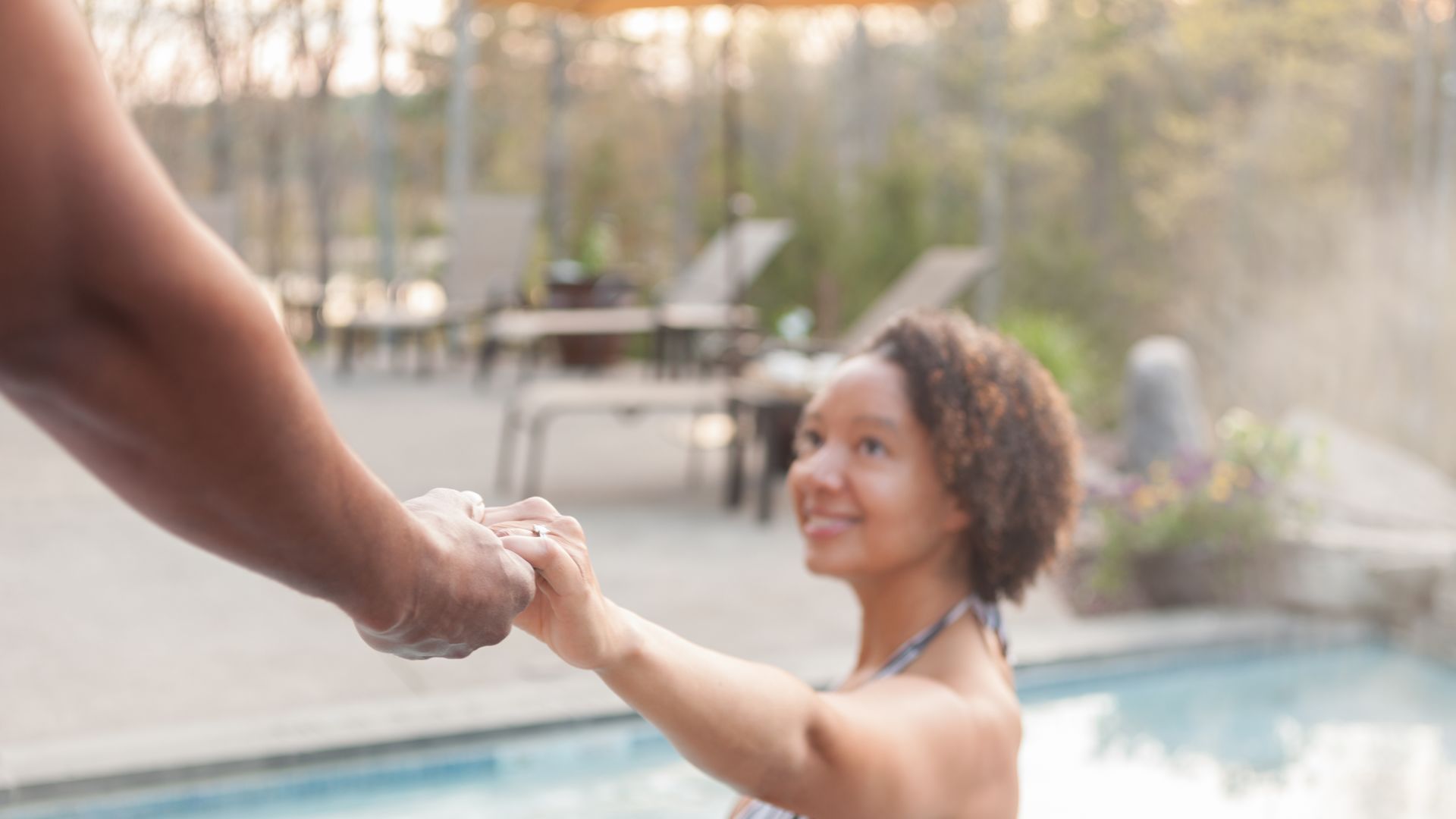 A woman smiling and holding a man's hand pulling him into an outdoor whirlpool