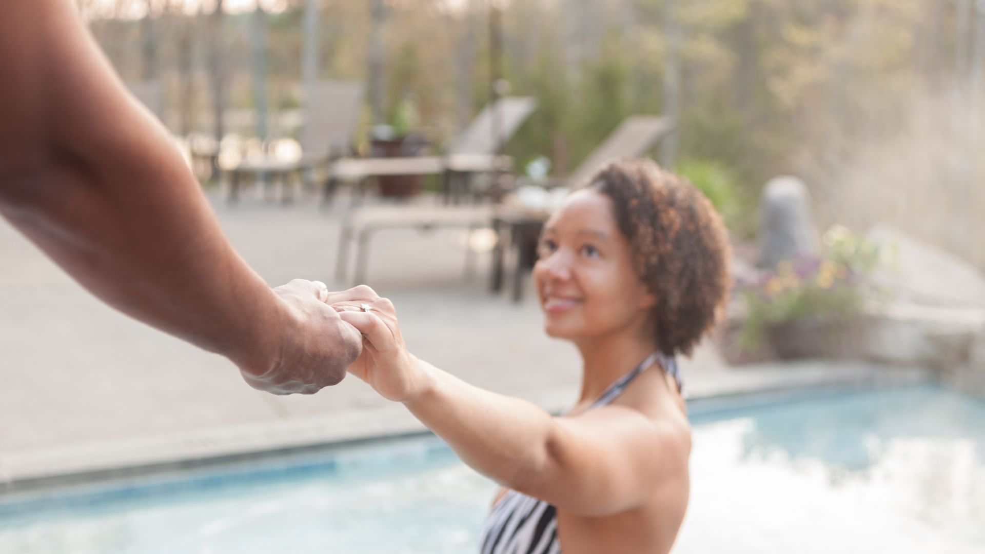 A woman smiling and holding a man's hand pulling him into an outdoor whirlpool
