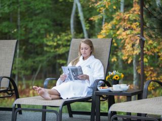 A woman wearing a spa robe and reading a magazine in a Chaise Lounge on the Sun Terrace at The Lodge at Woodloch