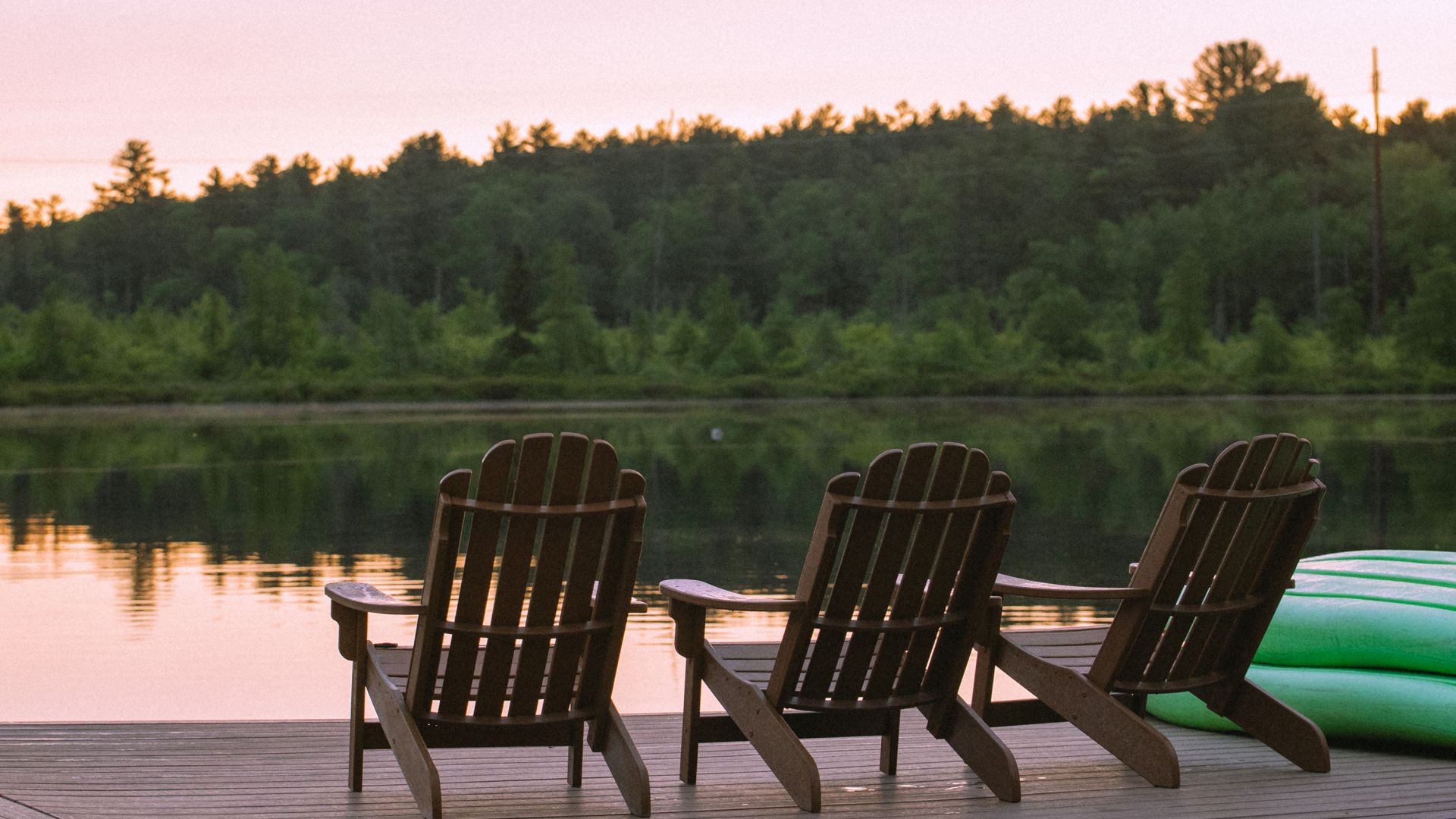 Three Adirondack chairs on a dock facing the lake at sunset at The Lodge at Woodloch