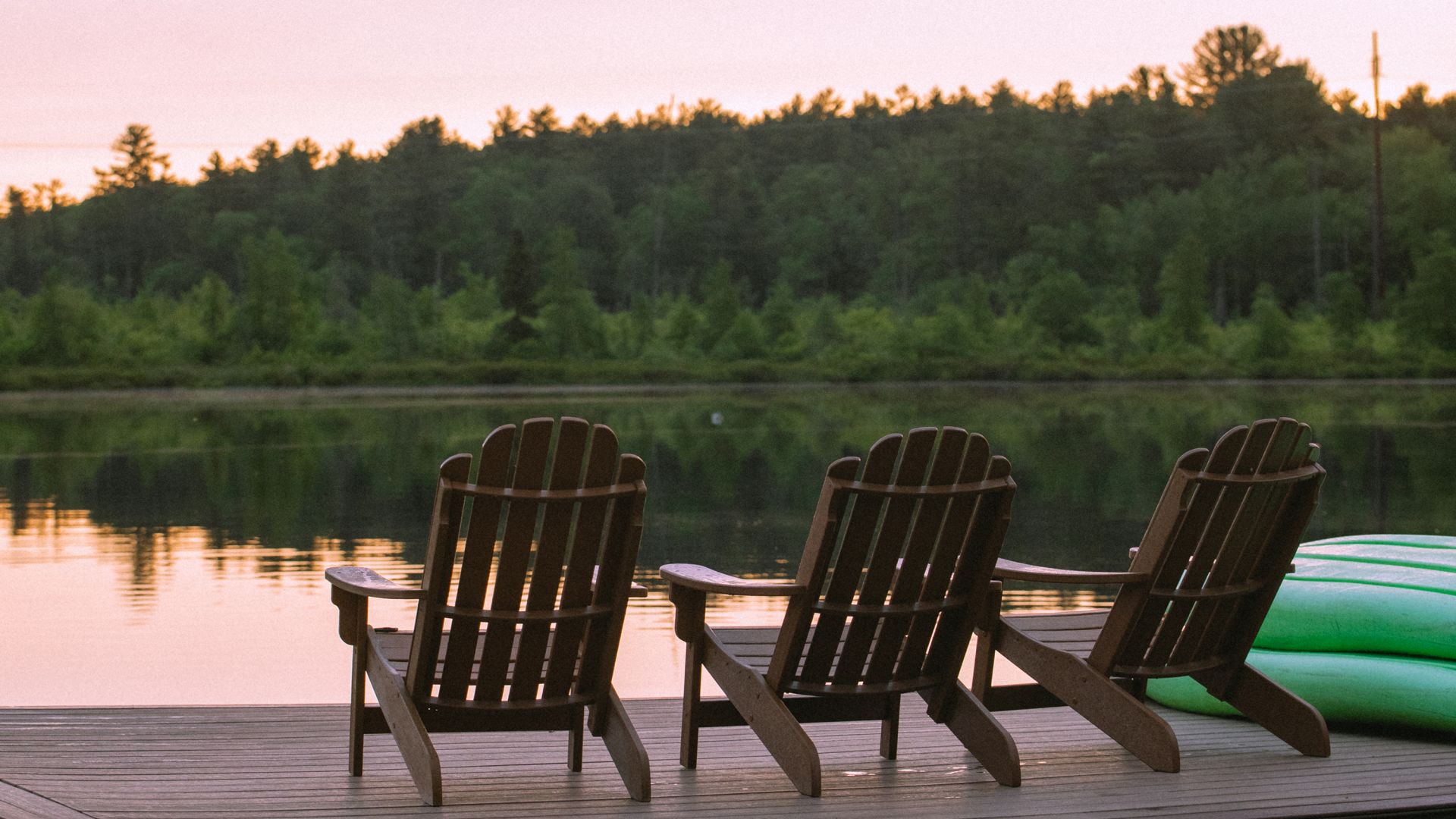 Three Adirondack chairs on a dock facing the lake at sunset at The Lodge at Woodloch