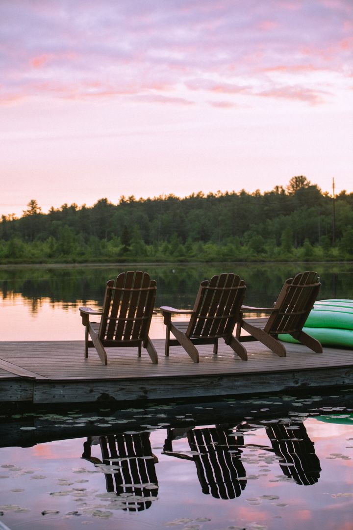 Sunset over a lake with adirondack chairs on a dock in the foreground.