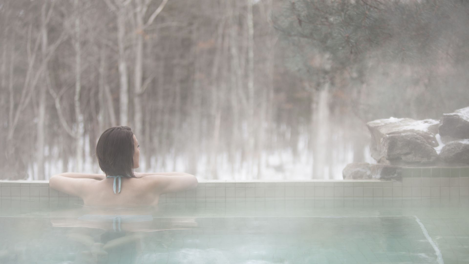 Solo woman looking at the forest from the Horizon Edge Outdoor Whirlpool in Winter at The Lodge at Woodloch